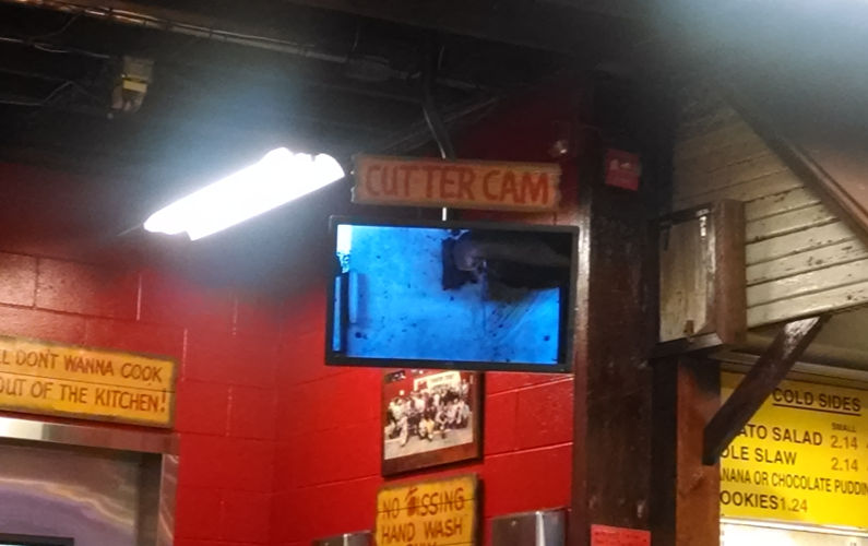 An Overhead TV Called Rudy's BBQ "Cutter Cam" Displaying Meat Cutting