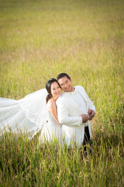 Nadia in a White Wedding Dress Holding JM in a White Tuxedo Jacket and Dark Blue Jeans From Behind in a Grass Field by Ching Hua Bridal Art