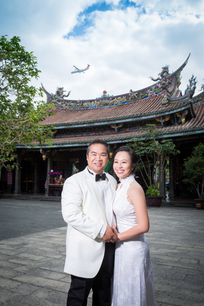 Nadia in a White Dress Hand in Hand with JM in a Black and White Tuxedo with a Plane Overhead at Lungshan Temple By Ching Hua Bridal Art