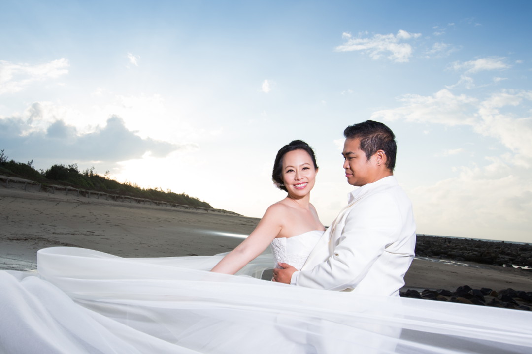 Barefoot Nadia in a Flowing White Wedding Dress Being Held By JM in a White Tuxedo Shirt and Dark Blue Jeans on the Beach by Ching Hua Bridal Art